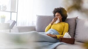 sick-woman-sitting-on-couch-with-kleenex-and-blanket