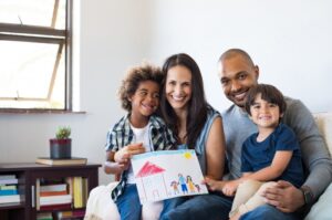 multi-ethnic-family-sitting-on-couch-with-drawing-of-a-house-and-family